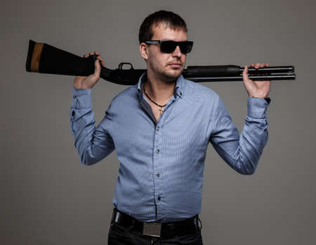 Serious man - gangster in sunglsees poses holding shoot-gun in his handsの写真素材