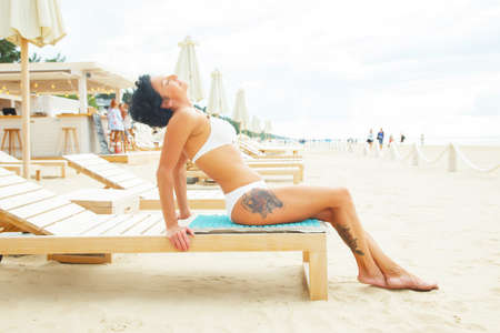 Middle age woman with black hair and tattoe on her leg sitting on a beach sofa.の写真素材