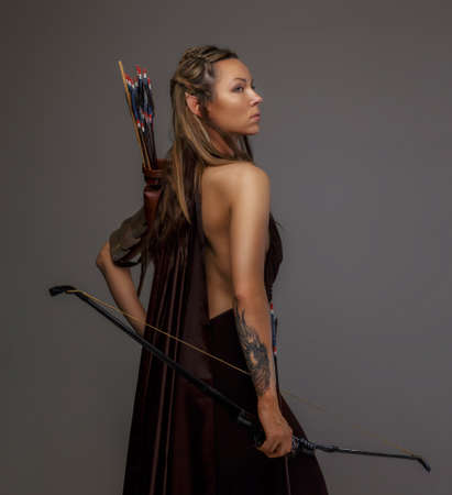 Beautiful elf woman with bow in her hand. Isolated on gray.の写真素材