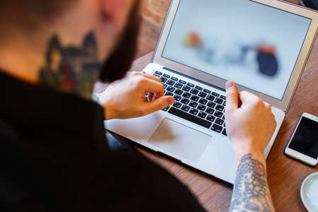 Tattoed man with beard work with laptop during a lunch.の写真素材