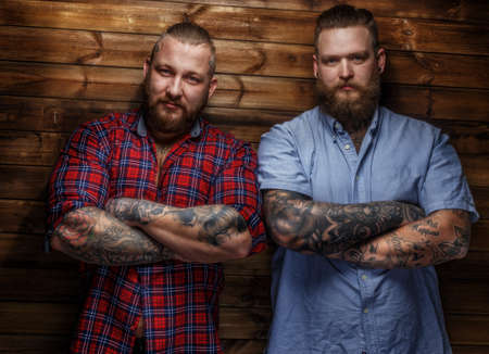 Two brutal huge males with beards in t-shirts posing in front of wooden wallの写真素材
