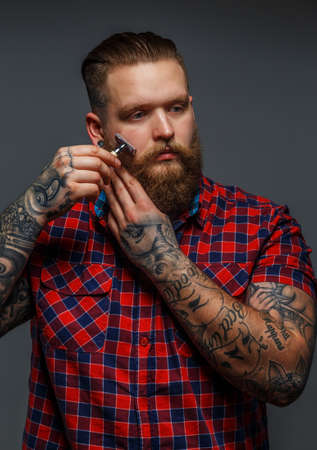 Huge brutal man with tattoo shawing his beard with a razorの写真素材
