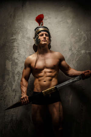 Muscular warrior with sword and helmet posing in front of concrete wallの写真素材