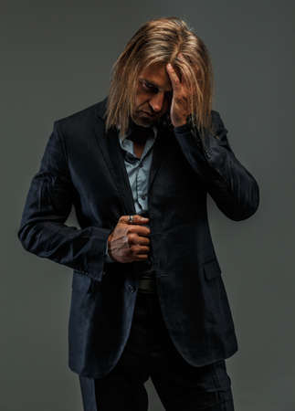 Portrait of handsome long-haired stylish man in dark grey suit. Isolated on gray background.の写真素材