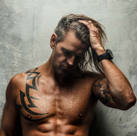 Portrait of handsome long-haired man with naked torso. Isolated on gray background. Tattoed male body.の写真素材