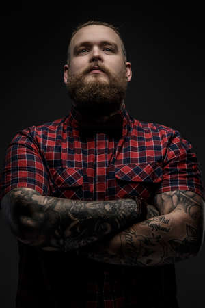 Man with beard in color shirt and tattooes on his hands posing in studio. Isolated on black.の写真素材