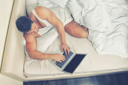 Young man using laptop at the bedtimeの写真素材