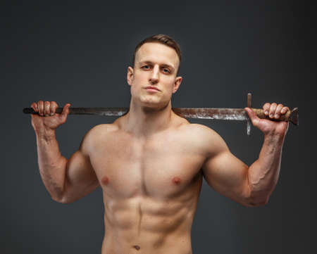Man with naked torso holds sword isolated on grey.の写真素材