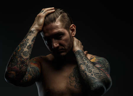 Portrait of a man with naked torso and tattooes. Dark and deep shadows.の写真素材