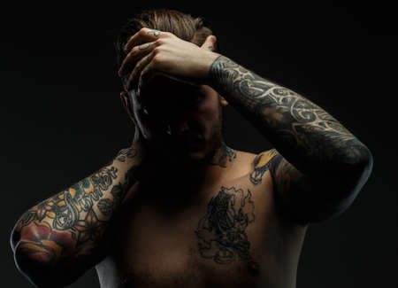 Portrait of a man with naked torso and tattooes. Dark and deep shadows.の写真素材