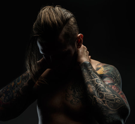 Portrait of a man with naked torso and tattooes. Dark and deep shadows.の写真素材