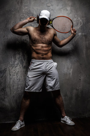 Male in white shorts with tennis racket over grey wall.の写真素材