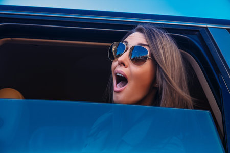 Young happy awesome woman in sunglasses looking from a carの写真素材