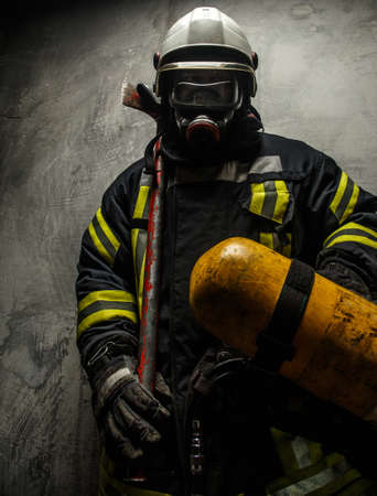 Firefighter in uniform with axe and oxygen on grey backgroundの写真素材