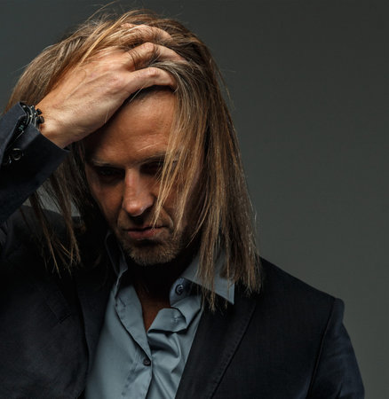 Portrait of handsome middle age long-haired stylish man in dark grey suit. Isolated on gray background.の写真素材