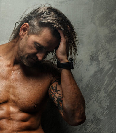 Portrait of handsome long-haired man with naked torso. Isolated on gray background. Tattoed male body.の写真素材
