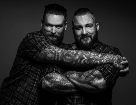 Two friends with tattos posing in studio. Black and white portrait