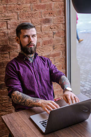 man with tattoo working with laptop in restaurantの写真素材