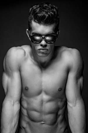 Portrait of awesome male model in sun glasses with naked muscular body. Isolated on dark grey background.の写真素材