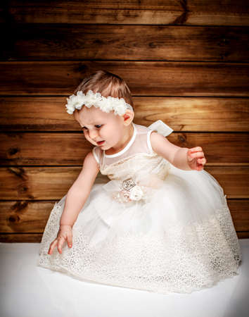 Emotional child in white dress over wooden wallの写真素材