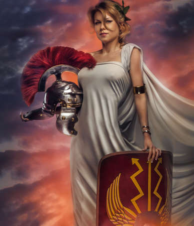 Middle age woman in white dress with roman armour holding shield and helmet. Sunset background.の写真素材
