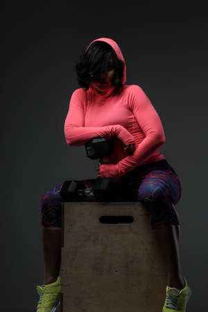 Attractive fitness woman in sportswear posing with dumbells in sudio on grey background