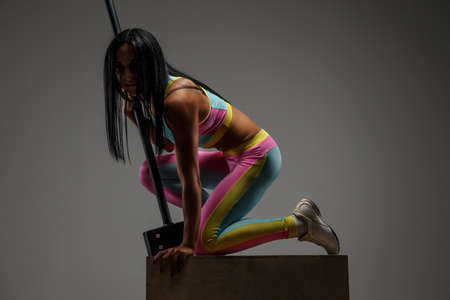 Woman in colorful sportswear standing on knee and holding hummer. Isolated on grey backgroundの写真素材