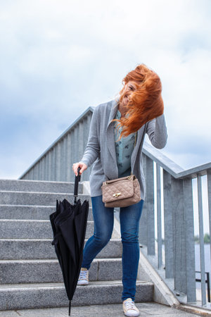 Red hair woman with ubbrella and casual clothes walking on street ladderの写真素材