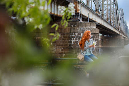 Redhead girl posing near old train bridge. Shoot throught green leafsの写真素材