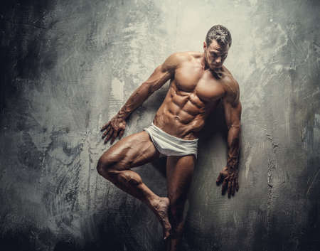 Muscular fitness model guy in white panties posing on grey background.の写真素材