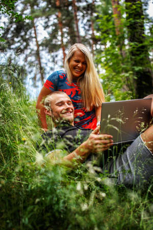 Man and woman with laptop lying on grass in the forest.の写真素材