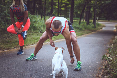 Man and woman in sportswear doing exercises and their dog on the forest road.の写真素材