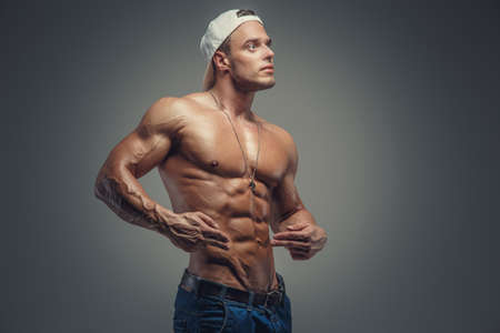 Shirtless muscular guy in blue jeans and white cap. Isolated on grey background.の写真素材