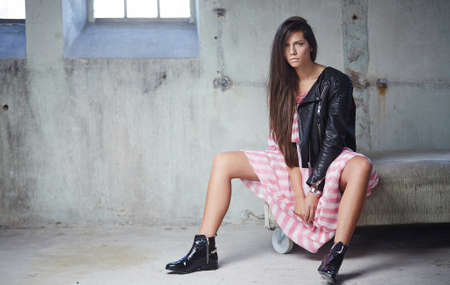 Sexy brunette in pink dress and leather jacket posing on camera.
