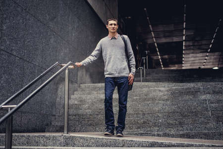 Student in blue jeans and grey jacket going down on steps.の写真素材