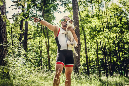 Sportsman in sportswear and sunglasses with his little dog in the green forest.の写真素材
