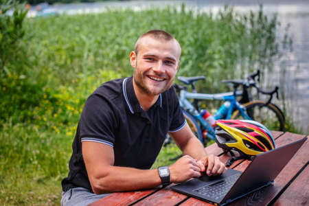 Smiling man sitting at table on lake shore with sport bycicles on background.の写真素材