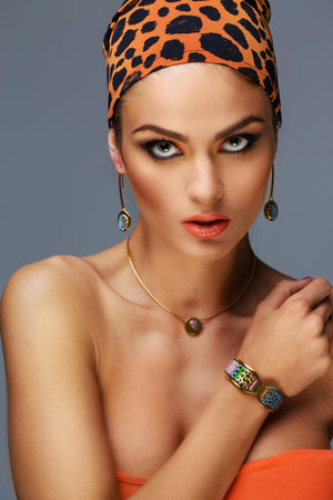 Portrait of woman with exotic make up. Bracelets on hands and orange leopard pattern on bandana.