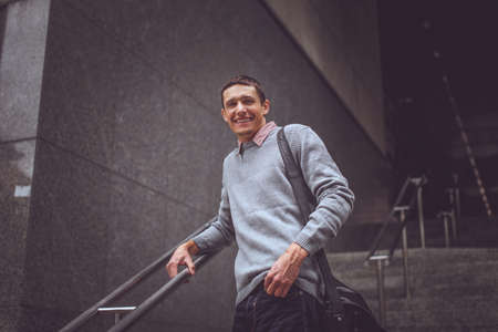 Student in blue jeans and grey jacket going down on steps.の写真素材