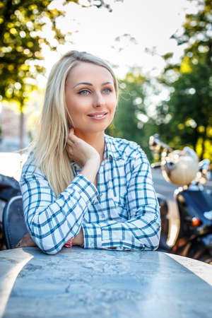 Smiling girl with long blond hair in t-shirt sitting at the table outside.の写真素材