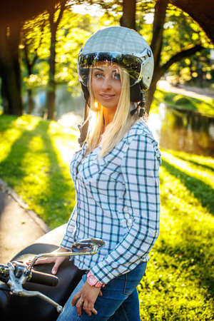 Casual smiling blond woman in moto helmet posing on scooter on nature background.の写真素材