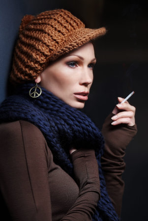 Portrait of woman with cigarette in brown winter head and blue scarf.の写真素材