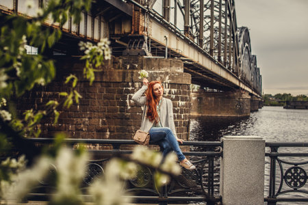 Shoot through green leafs of redhead casual young woman. Train bridge on background.の写真素材