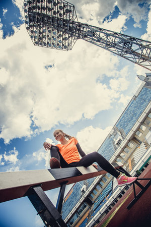 Slim woman in sportswear doing exercises on the stadium over blue sky with white clouds.の写真素材
