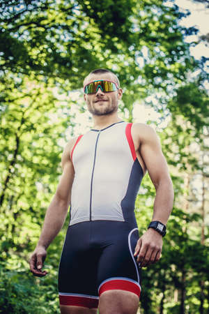 Running man in sportswear and sunglasses doing exercises in the forest.