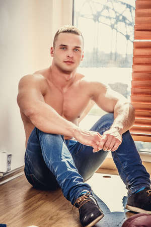 Awesome shirtless man in blue jeans sitting near window.の写真素材