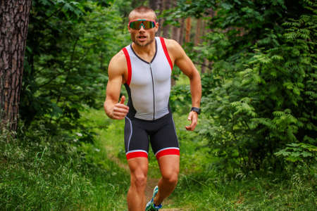 Running man in sportswear in green summer forest.の写真素材