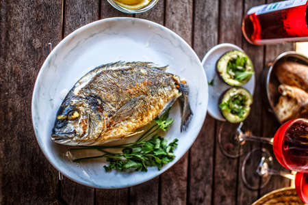 Grilled fish on white plate and glass of red wine.の写真素材