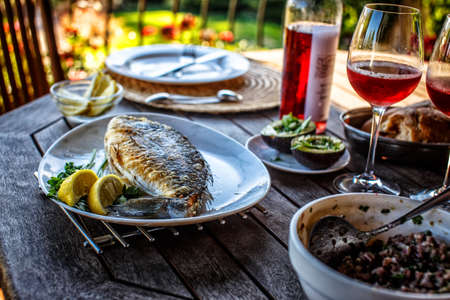 Grilled fish on white plate and glass of red wine.の写真素材