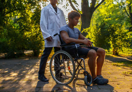 Guy in wheelchair resting in the park with his doctor.の写真素材